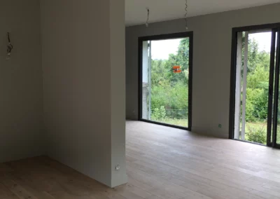 Pièce rénovée lumineuse avec parquet clair, murs gris et grandes baies vitrées.