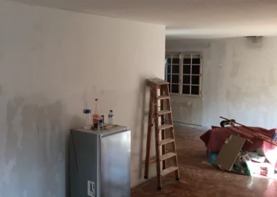 Pièce en cours de rénovation avec murs préparés, escabeau et matériel de chantier.